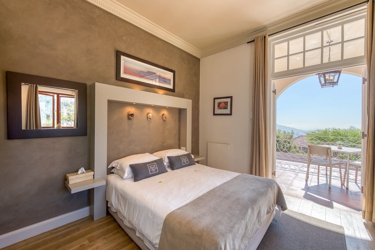 A bedroom with a large bed, a window with curtains, a framed picture on the wall, and a view of the outdoors.