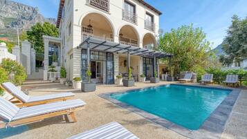 A poolside area with lounge chairs, a pergola, and a mountain backdrop.
