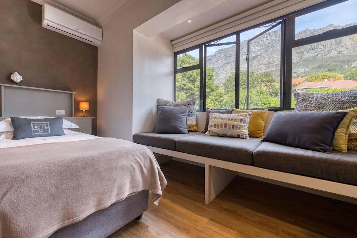 A modern hotel room with a large bed, a bench with cushions, and a view of the outdoors.