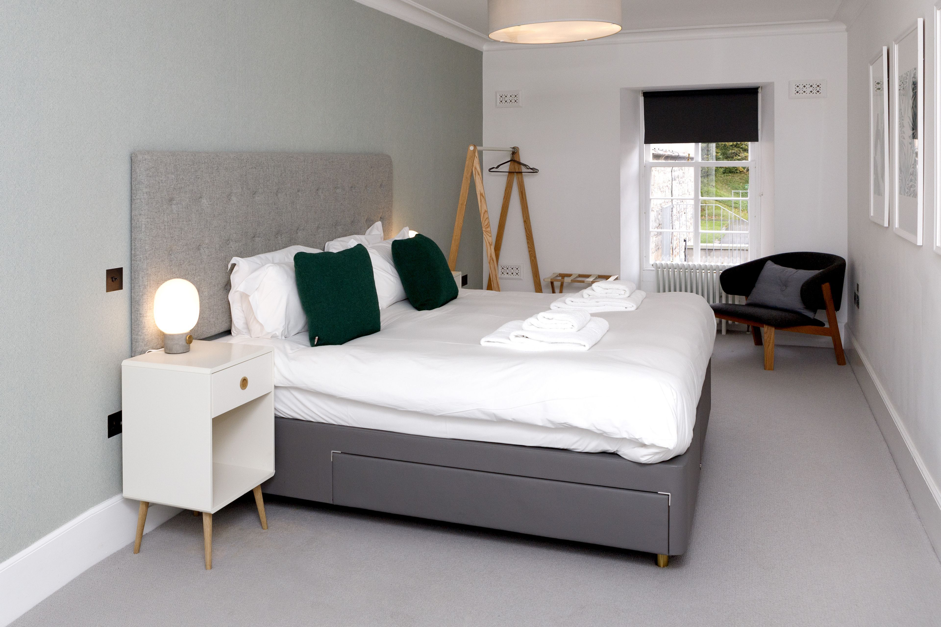 Un dormitorio moderno con una cama grande, mesitas de noche, una silla y un radiador.