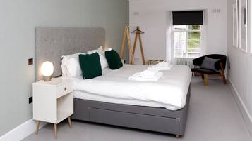 Un dormitorio moderno con una cama grande, mesitas de noche, una silla y un radiador.