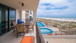 A balcony with a view of the beach, a pool, and outdoor seating.