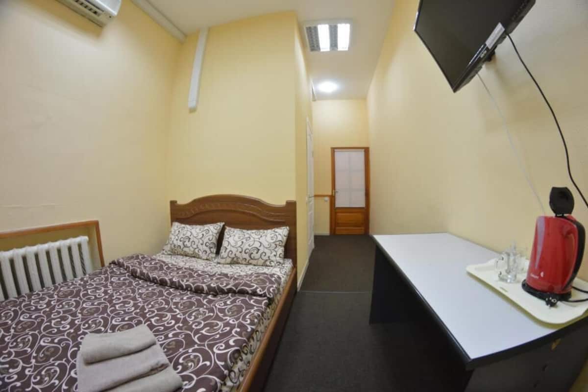 A small, compact room with a bed, a desk, and a TV mounted on the wall.
