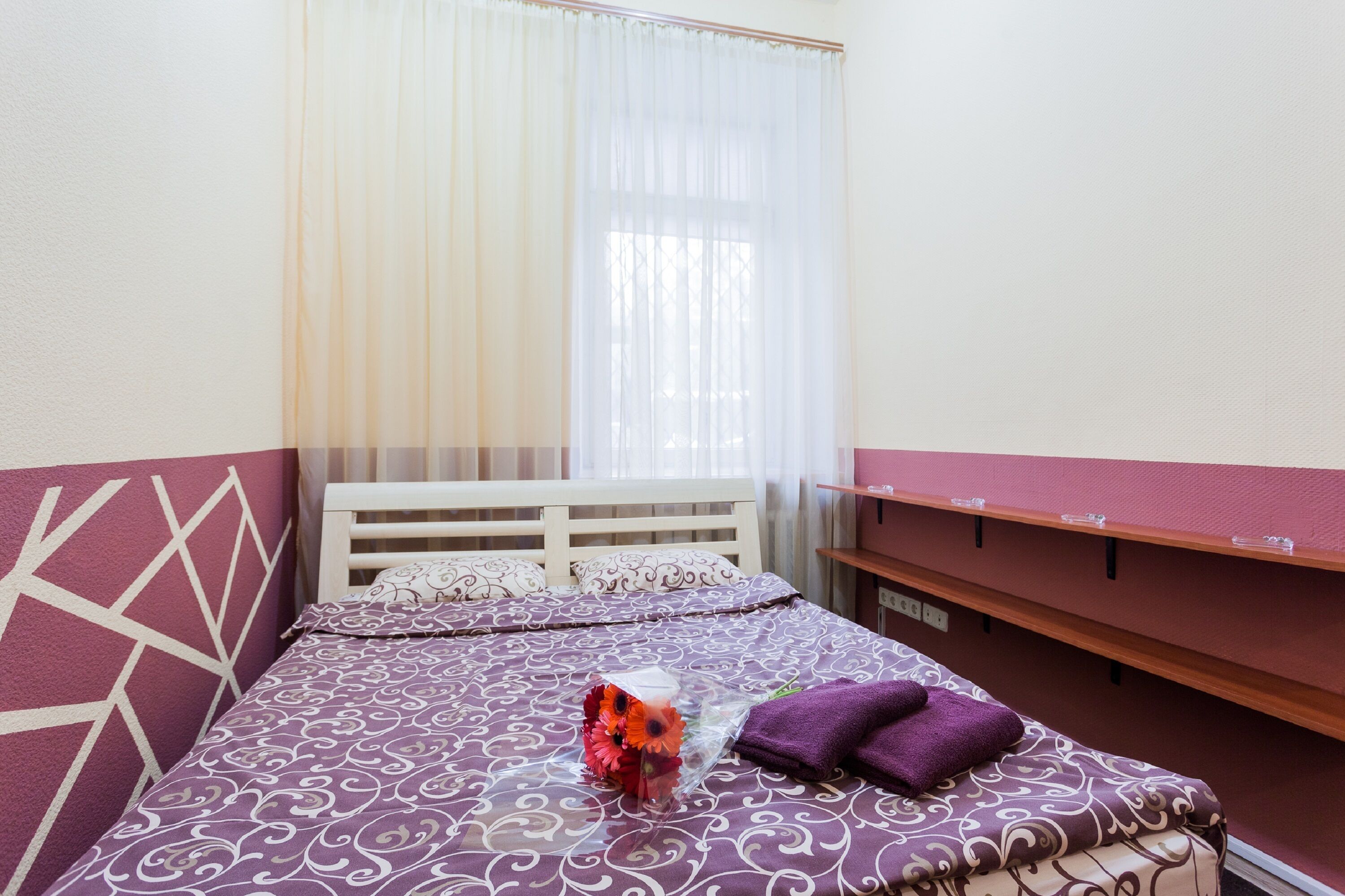 A neatly made bed with a patterned bedspread, a purple pillow, and a decorative flower arrangement.
