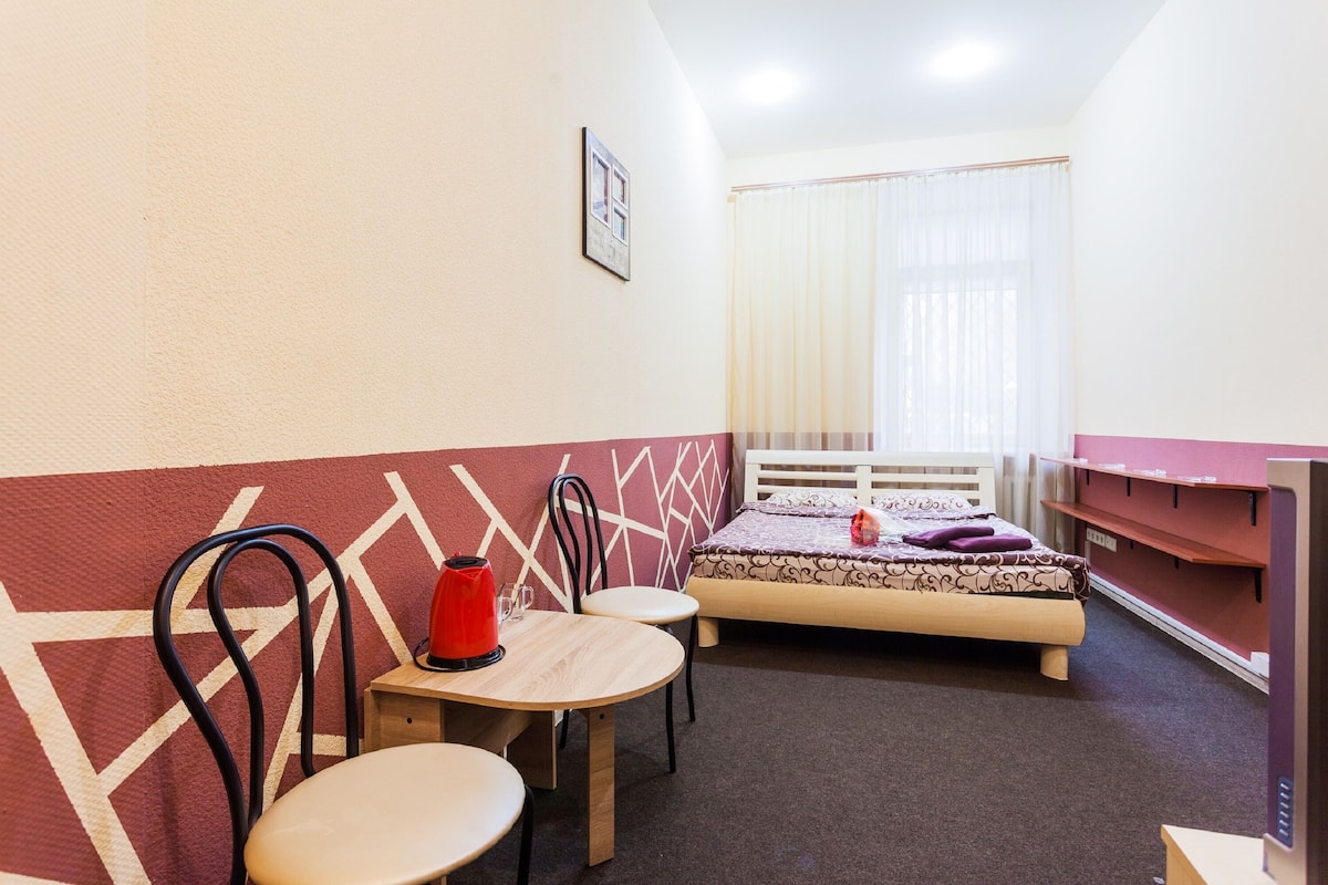 A small, cozy room with a bed, a table with chairs, and a TV.
