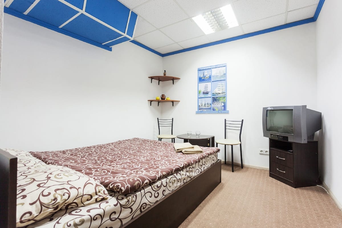 A bedroom with a bed, a desk, a chair, a television, and a bulletin board.