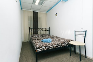 A single bed with a patterned bedspread, a chair, a window with curtains, and a wall-mounted light switch. - Mini-hotel in the heart of Kiev (Kyiv)
