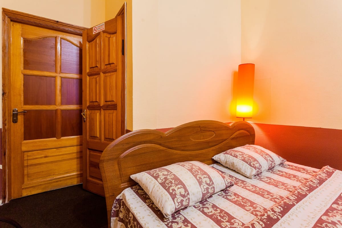 A bedroom with a wooden door, a bed with patterned bedding, and a wall-mounted light.