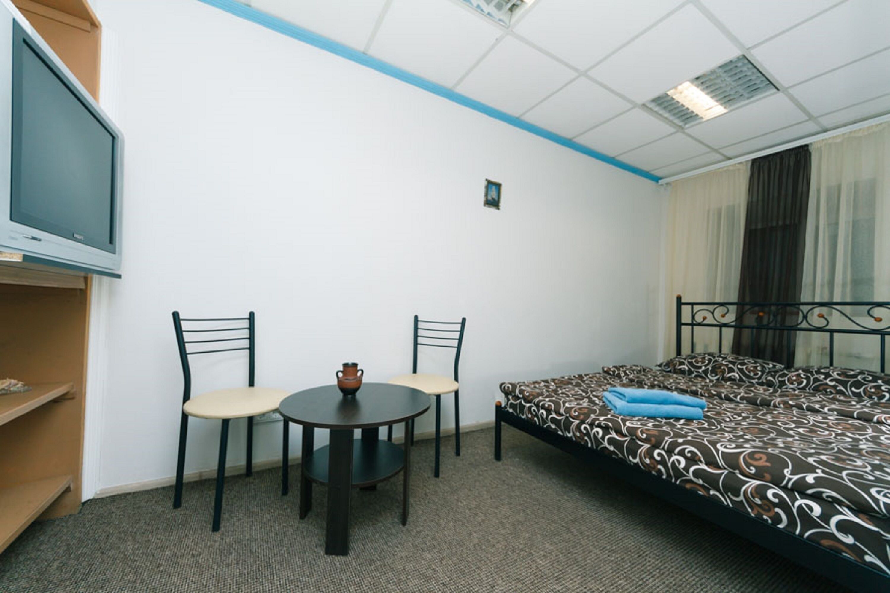 A small, neatly arranged room with a bed, two chairs, a small table, and a television.