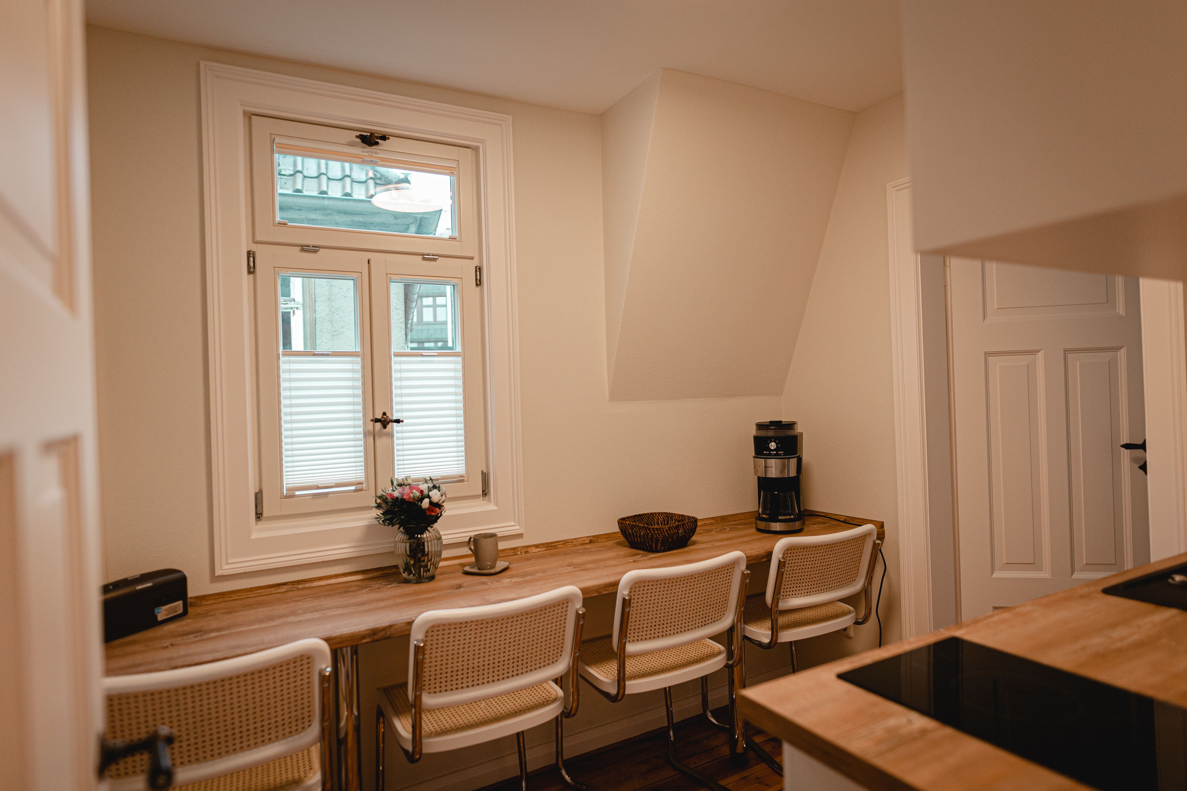 A kitchen with a wooden countertop, four wicker chairs, a coffee maker, and a window with blinds.