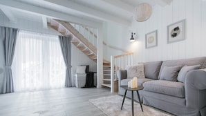 Un salon spacieux avec un canapé gris, une petite table d’appoint, un tapis moelleux et un escalier menant à l’étage supérieur.