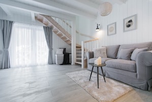 A spacious living room with a grey sofa, a small side table, a fluffy rug, and a staircase leading to an upper floor.