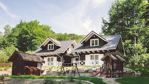 Une maison à deux étages, avec un chemin de pierre menant à l’entrée, entourée d’une végétation luxuriante et d’un petit étang.
