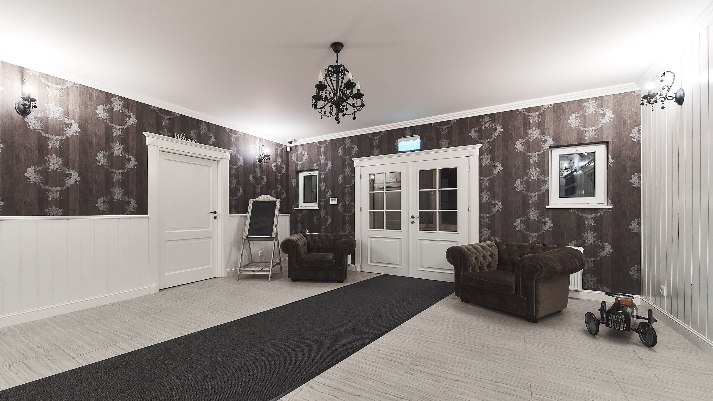 Una habitación amplia con alfombra negra, dos sillones, una mesita, una lámpara decorativa y una puerta con ventanal.