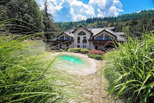 A house with a swimming pool, surrounded by greenery and a forested hillside.