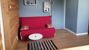 A room with a red sofa, a small round table, a striped rug, and a door with a small Christmas tree decoration. - Apartment in Les 2 Alpes. Snow front. 4 people max. (Mont-de-Lans)