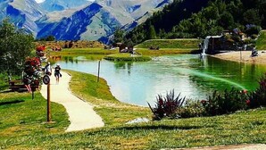 A lakeside path with a view of mountains and a waterfall. - Apartment in Les 2 Alpes. Snow front. 4 people max. (Mont-de-Lans)