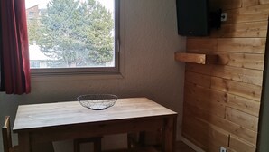 A room with a wooden table, a bench, a window with a view of trees, and a mounted TV on the wall. - Apartment in Les 2 Alpes. Snow front. 4 people max. (Mont-de-Lans)