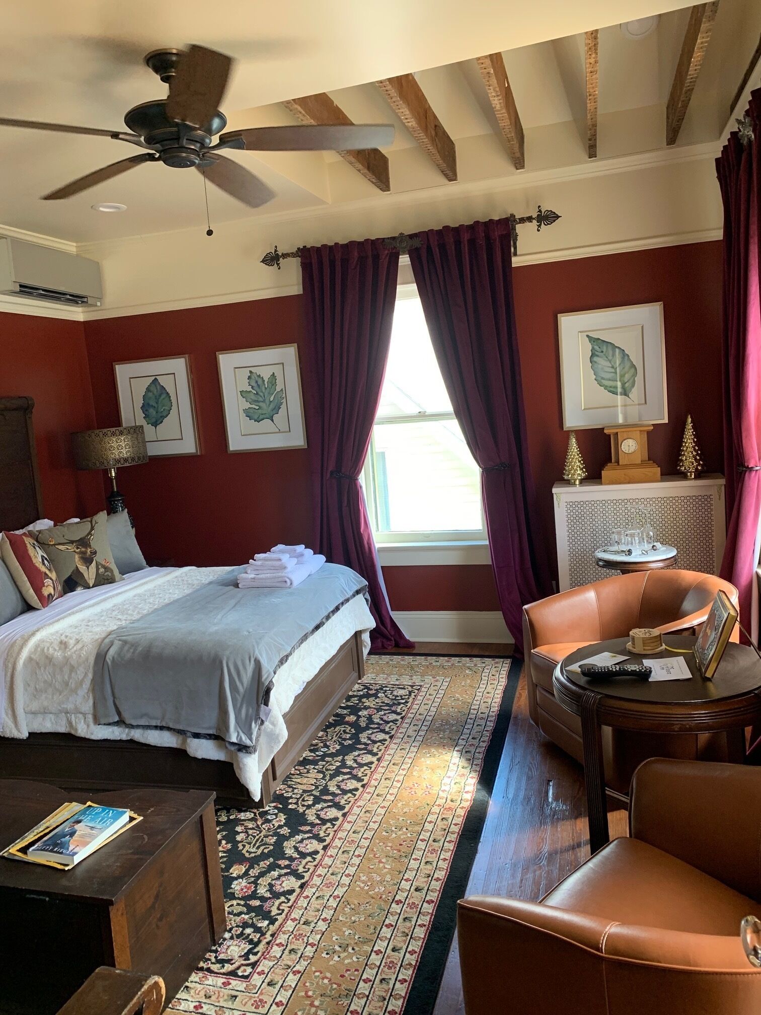 A bedroom with a bed, a desk, a chair, a ceiling fan, and a window with curtains.