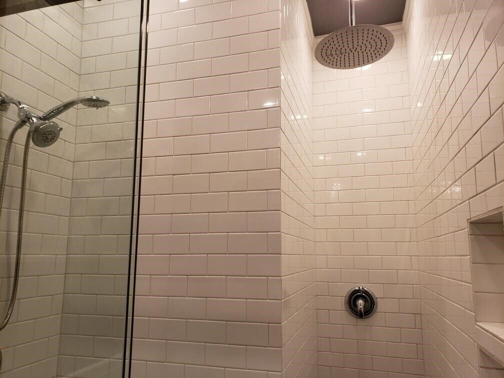 A shower with white tiles and a glass door.