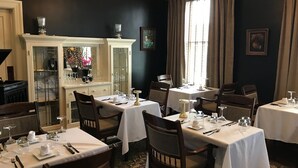 A dining area with multiple tables set for service, a chandelier, and a large window with curtains. - The Hygrade Inn (Emporium)