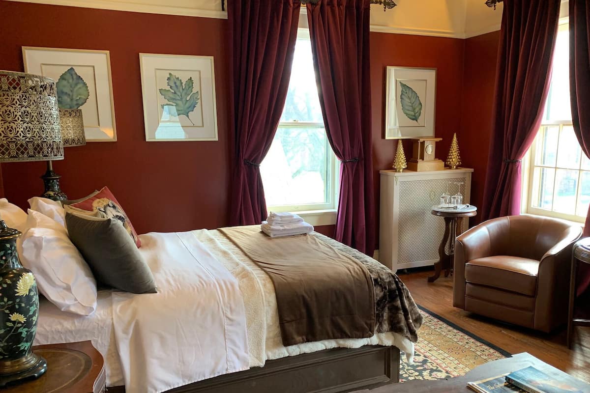 A well-appointed bedroom with a large bed, a leather armchair, and a small table with decorative items.