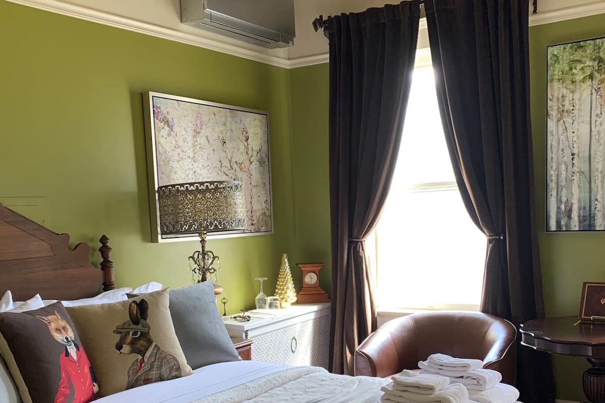 A hotel room with a bed, a chair, a desk, and a window with curtains.