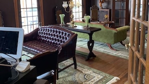 A spacious living room with a leather sofa, a green armchair, a wooden coffee table, and a television on a stand. - The Hygrade Inn (Emporium)