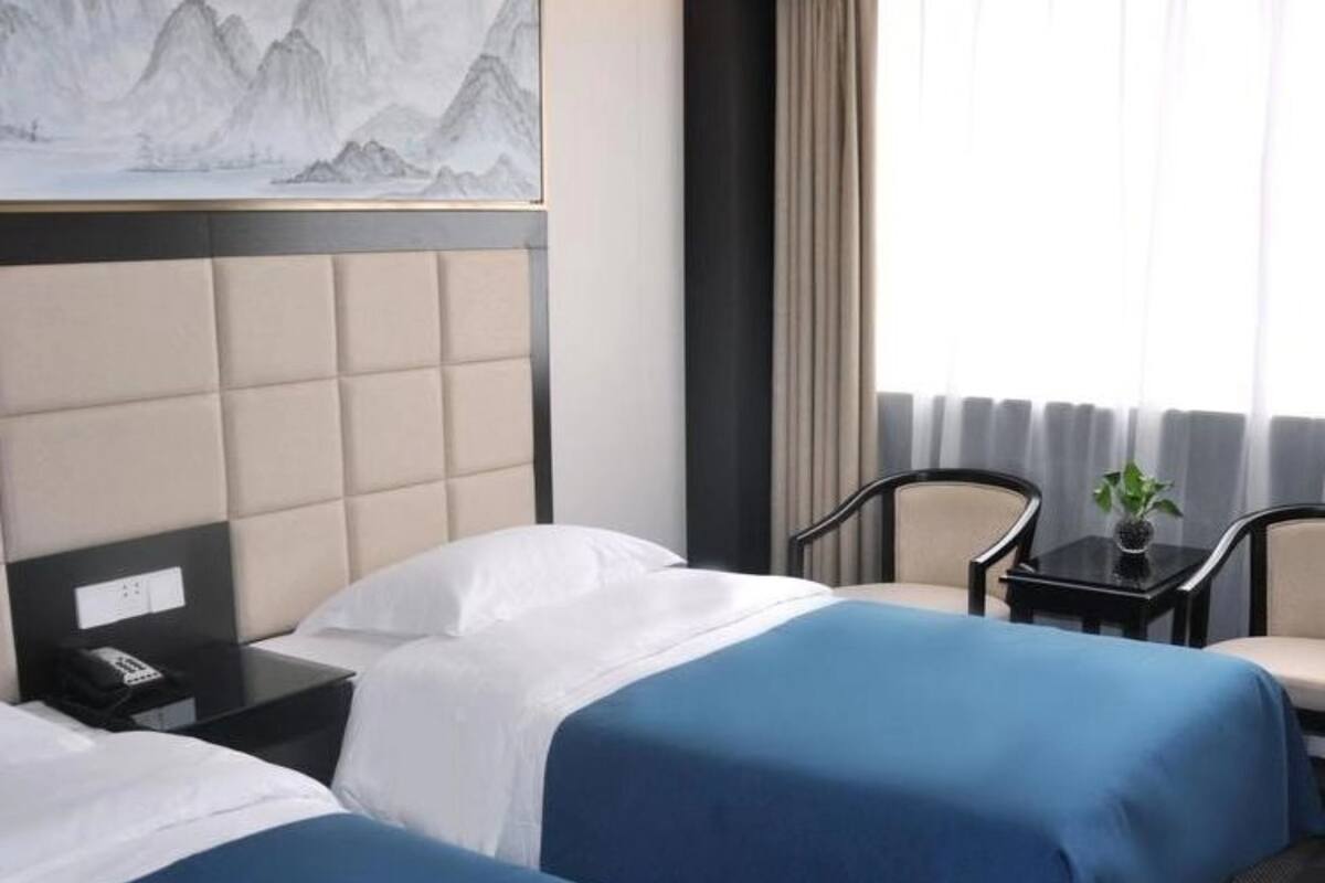 Een hotelkamer met twee bedden, een bureau met stoel, een schilderij aan de muur en een raam met gordijnen.