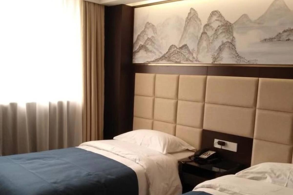 Hotelkamer met twee bedden, een hoofdbord met berglandschap en nachtkastje met telefoon, en een raam met gordijnen.