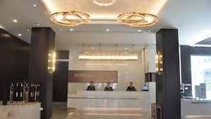 Un hall d’accueil moderne, avec un sol en marbre, un comptoir d’accueil et trois employés.