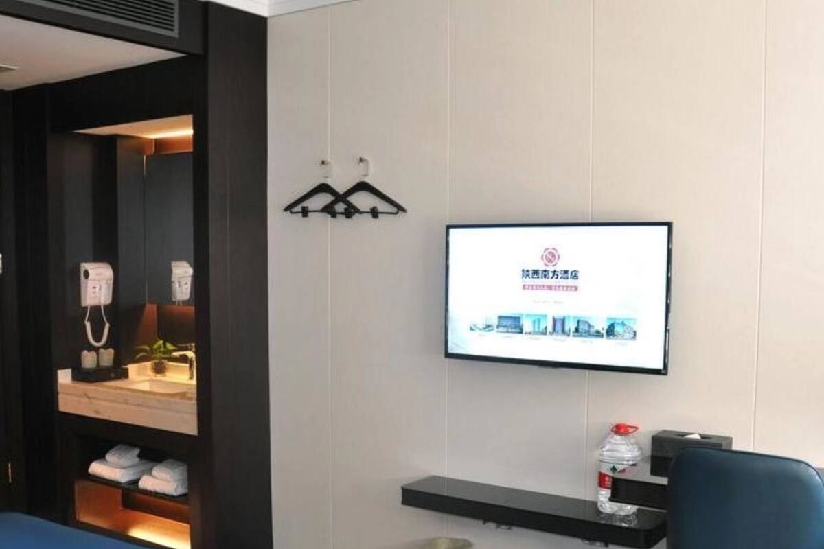 Een hotelkamer met een bed, een bureau met een computer, een televisie en een klein plankje met toiletartikelen.