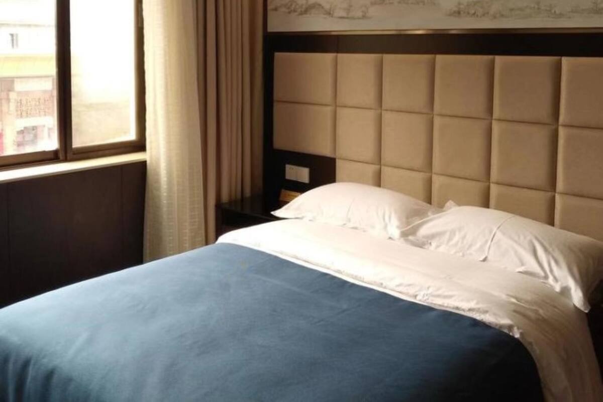 Hotelkamer met een groot bed, een hoofdbord met een gestoffeerd ontwerp, een raam met gordijnen, en een kunstwerk aan de muur.