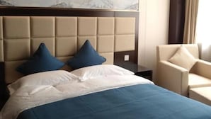 Une chambre d’hôtel avec un grand lit, deux oreillers, une tête de lit ornée d’un tableau représentant une montagne et un fauteuil.