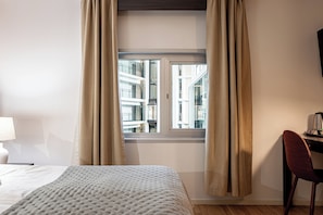A hotel room with a bed, a desk, a chair, and a window with curtains. - Injoy Park Hotel Solna (Solna)