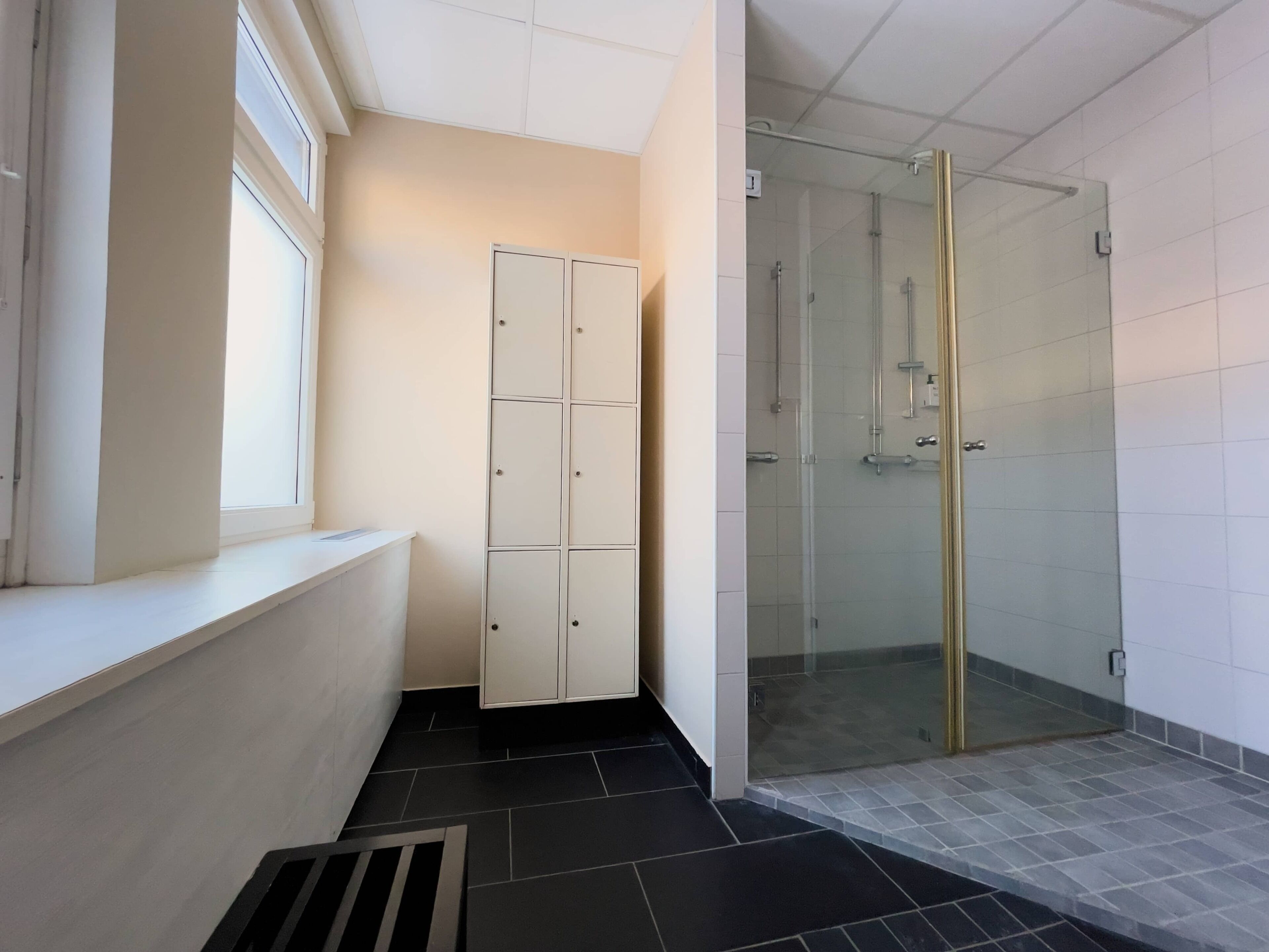 Un baño con ducha, un mueble blanco y una ventana.