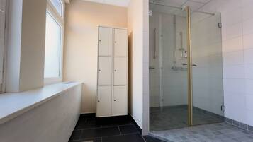 Un baño con ducha, un mueble blanco y una ventana.