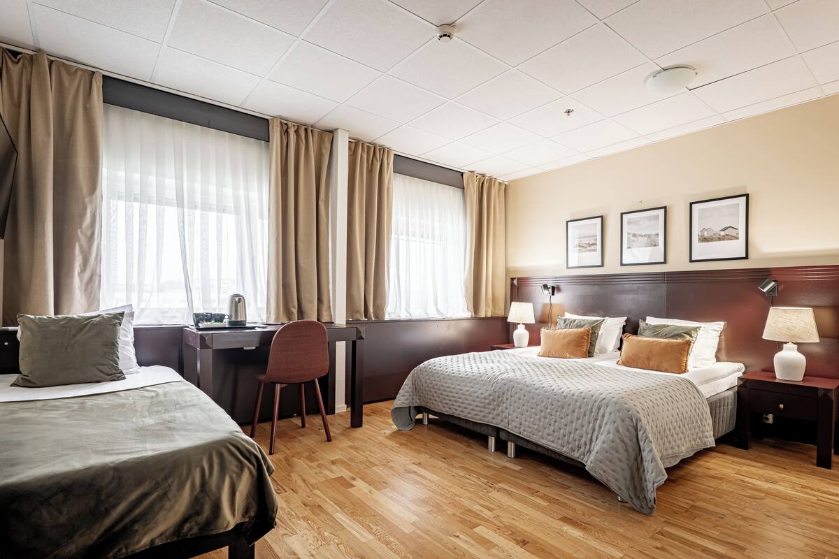 Habitación de hotel con dos camas, un escritorio, una silla y una mesita de noche con lámparas.