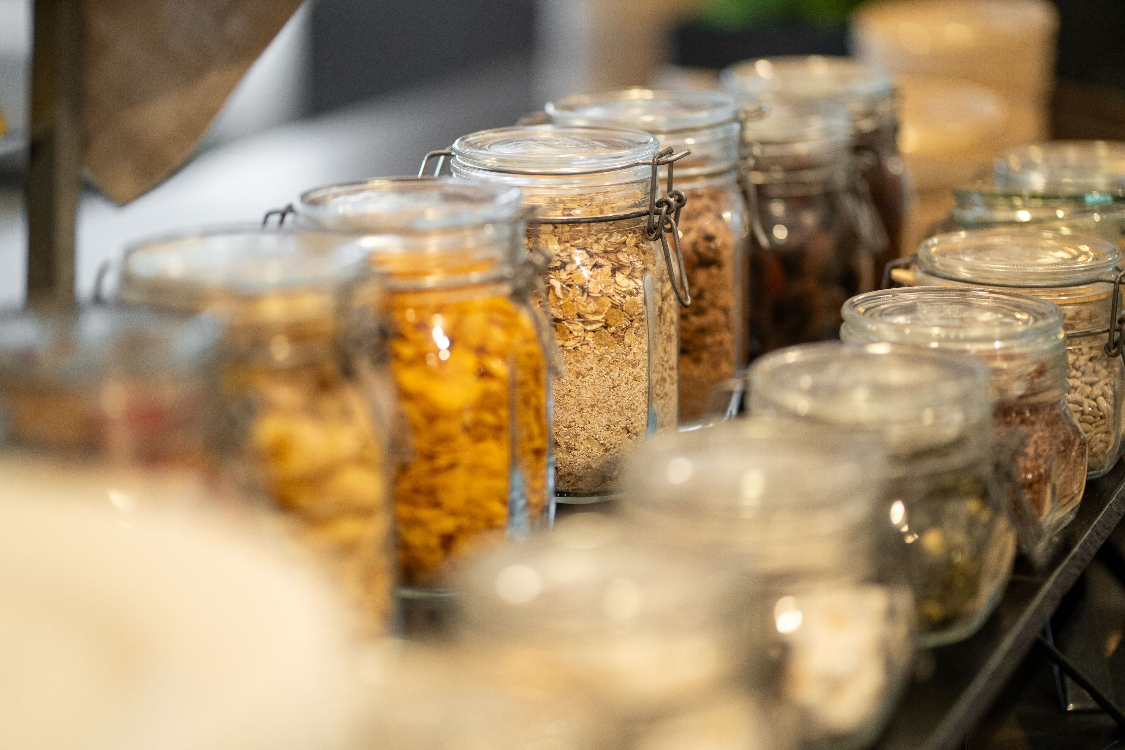 Una hilera de frascos de vidrio con cierres metálicos, que contienen diversos alimentos.