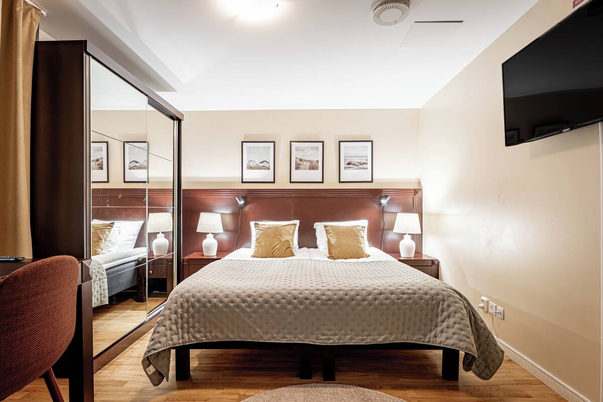 Habitación de hotel con una cama grande, lámparas de noche, un televisor de pantalla plana y cuadros en la pared.