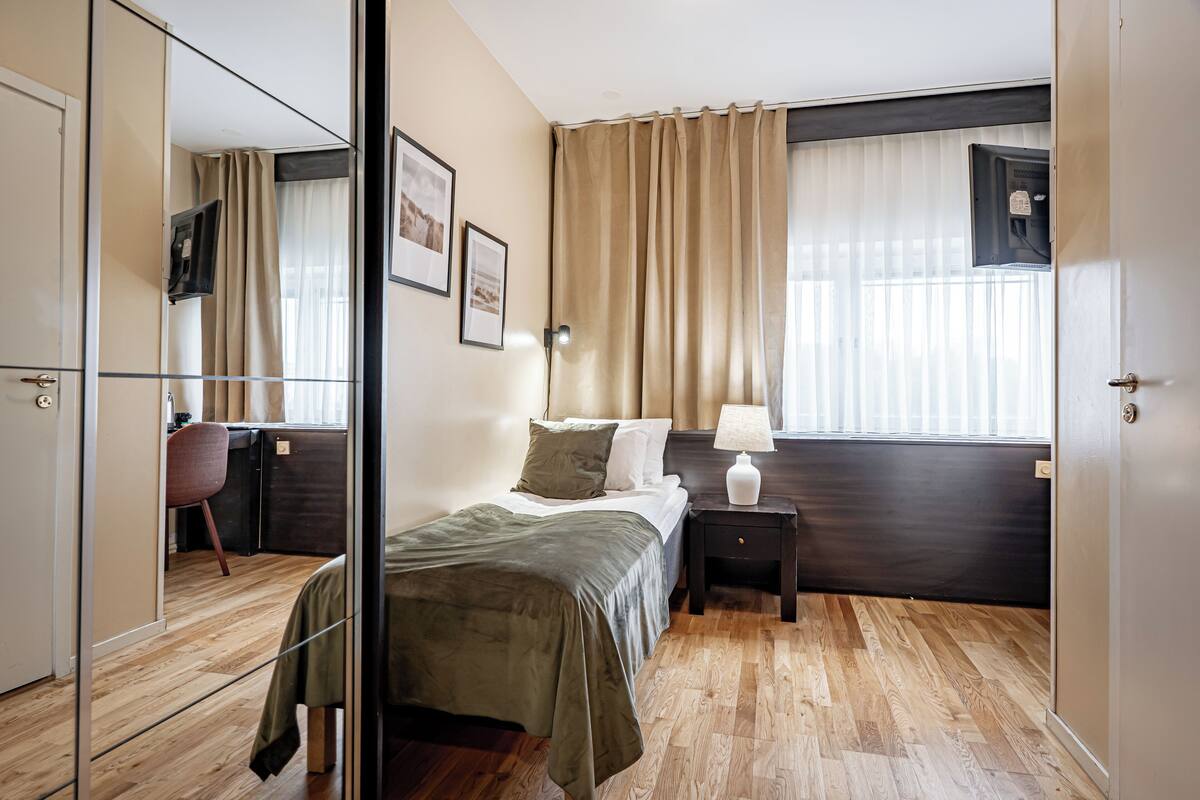 Un dormitorio con cama, mesita de noche, lámpara y espejo.