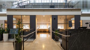 Een modern interieur met een trap die leidt naar een restaurantgedeelte, met glazen deuren, potplanten en een strakke, betegelde vloer.