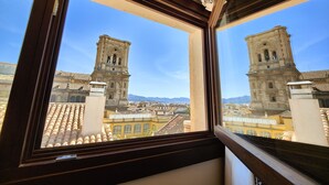A view through a window of a building with two prominent towers, a tiled roof, and a clear blue sky. - Toc Hostel Granada (Granada)