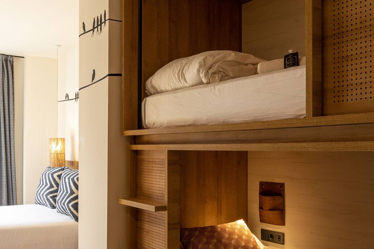 A bunk bed with a wooden headboard, a bedside table with a lamp, and a wall-mounted shelf.