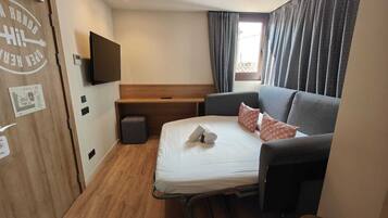 Habitació d'hotel senzilla amb un llit, escriptori, televisió penjada a la paret i una finestra amb cortines estampades.