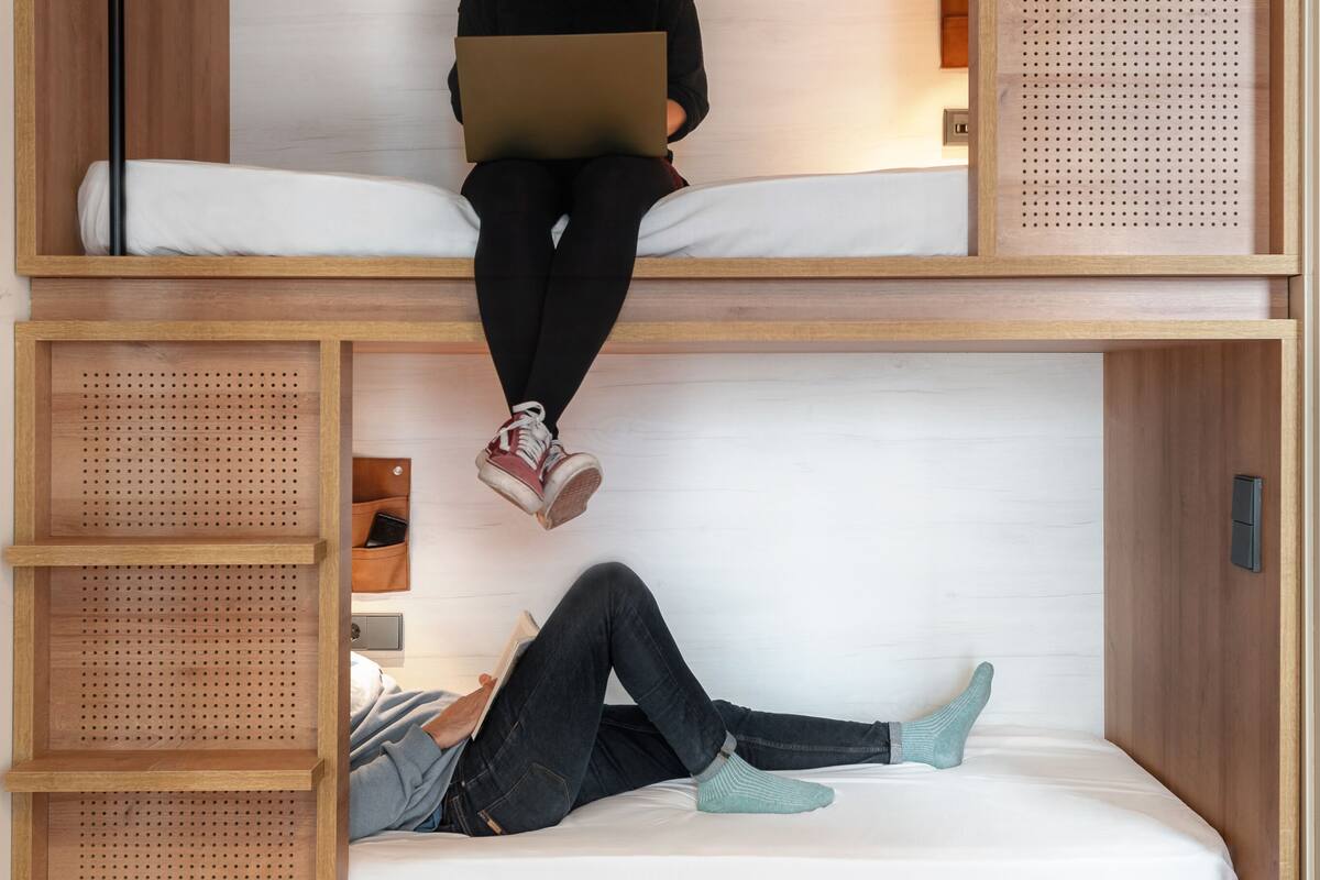 A bunk bed with a laptop on the top bunk and a person lying on the bottom bunk.