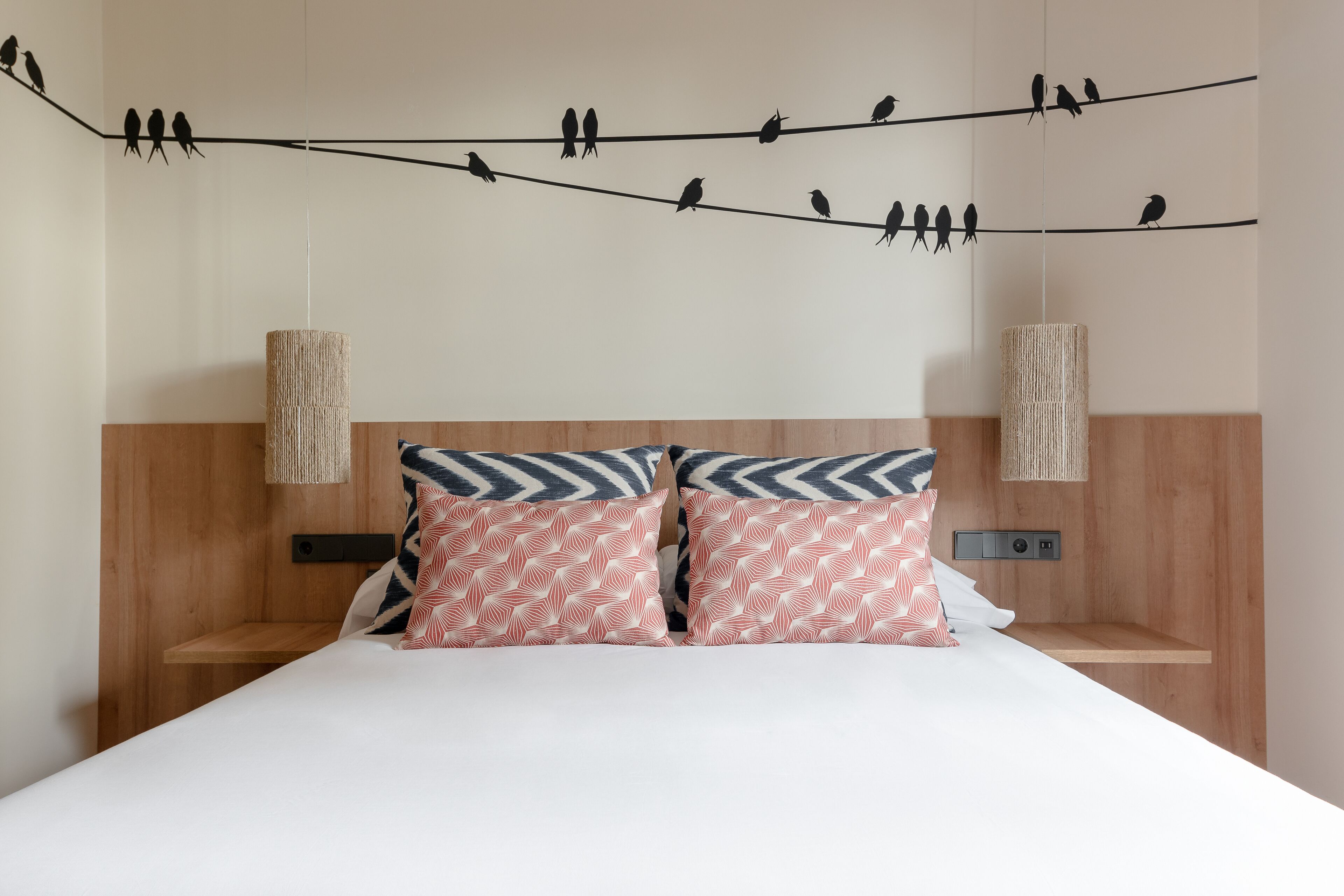 A bed with two pillows, a wooden headboard, and a wall-mounted light fixture.