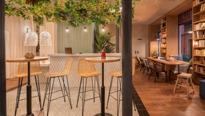 A cozy cafe with wicker chairs, a wooden table, and a bookshelf filled with books. - Toc Hostel Granada (Granada)