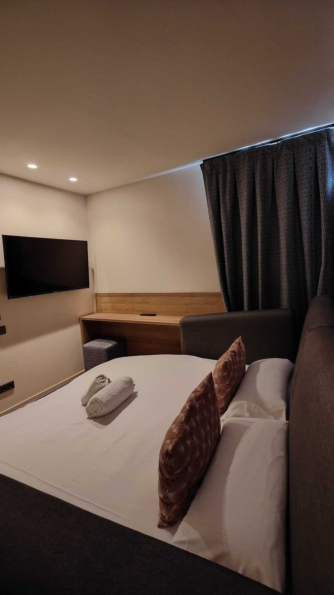 Een hotelkamer met een bed, een flatscreen televisie aan de muur, een houten bureau en een donkerblauwe bank.
