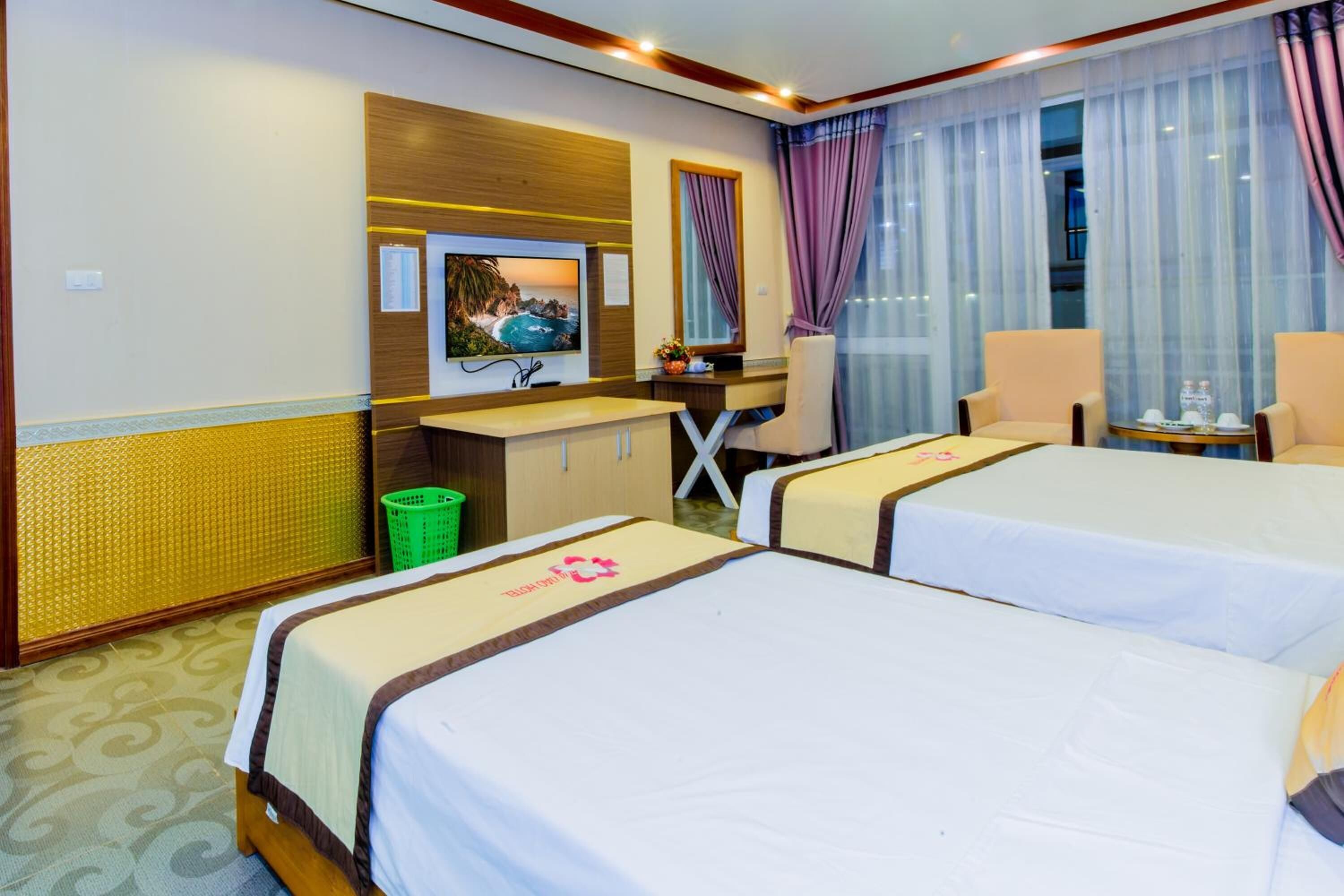 A hotel room with two beds, a desk, a chair, a TV, and a window with curtains.